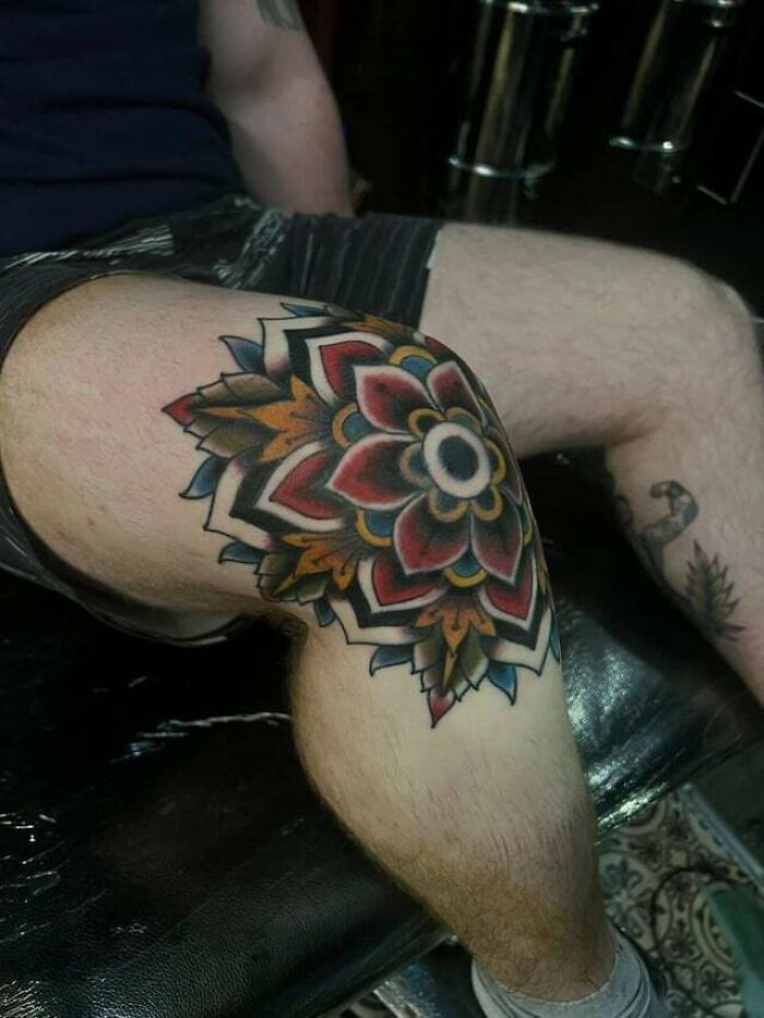 Vibrant knee tattoo with a geometric floral design in red, blue, and yellow hues.