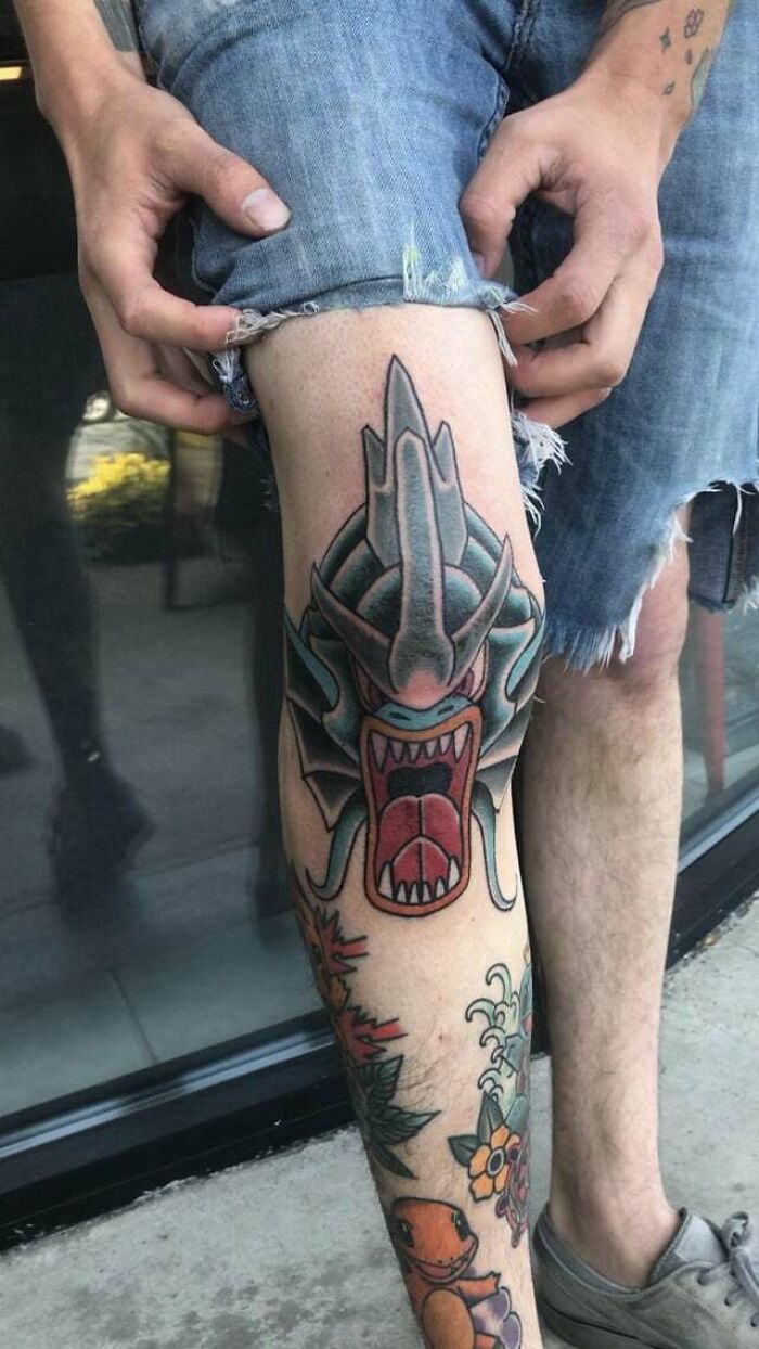 Knee tattoo featuring a colorful, fierce dragon design on a person's leg with denim shorts.