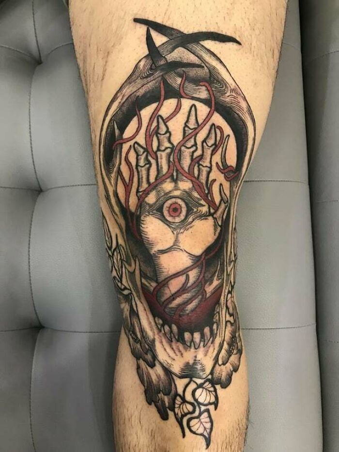Intricate knee tattoo design featuring an eye, flames, and skeletal fingers.