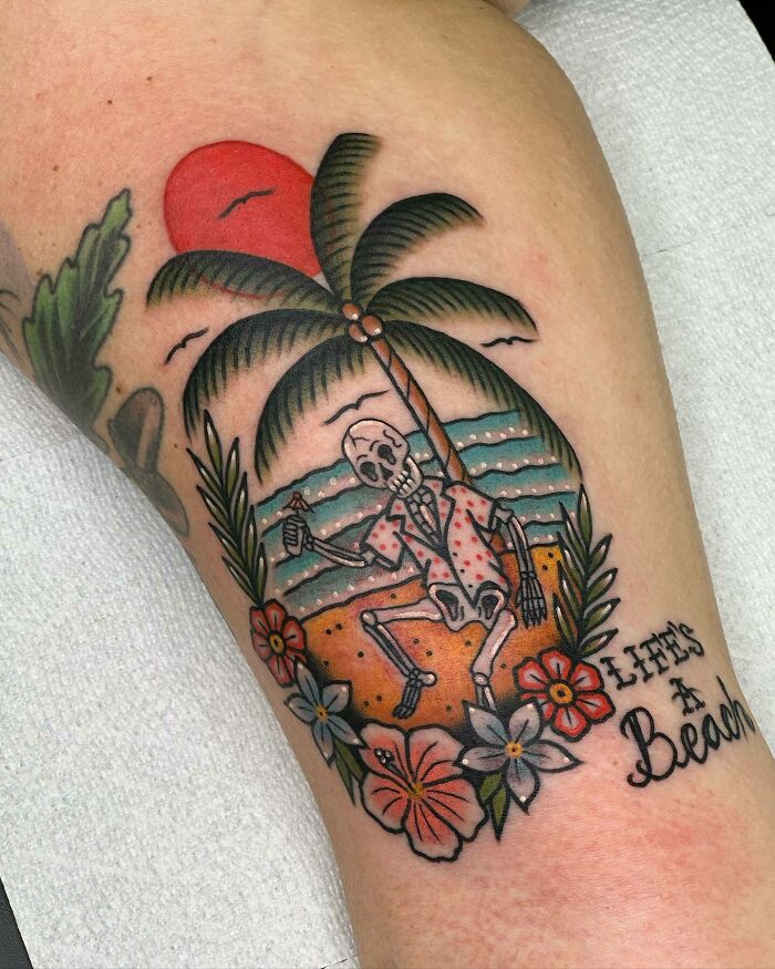 Knee tattoo featuring a skeleton under a palm tree, with a sunset and ocean waves in the background.