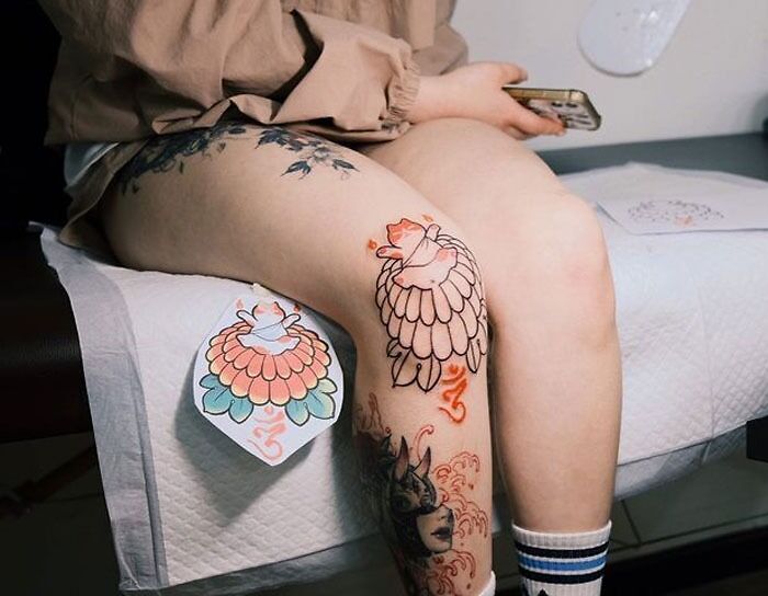 Person with decorative knee tattoos featuring colorful designs sitting on a chair.