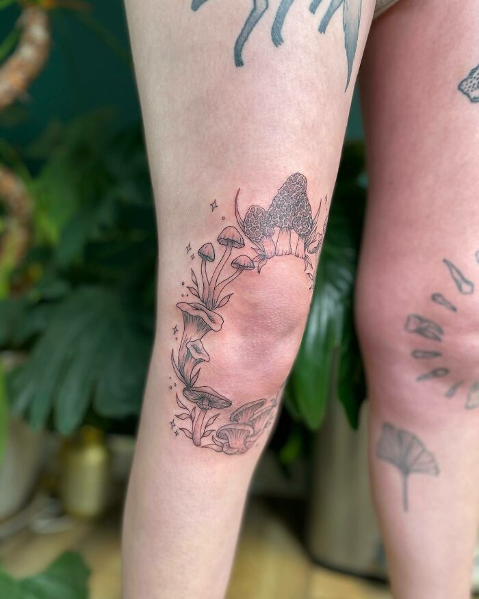 Floral knee tattoo featuring mushrooms and leaves, set against a natural background.