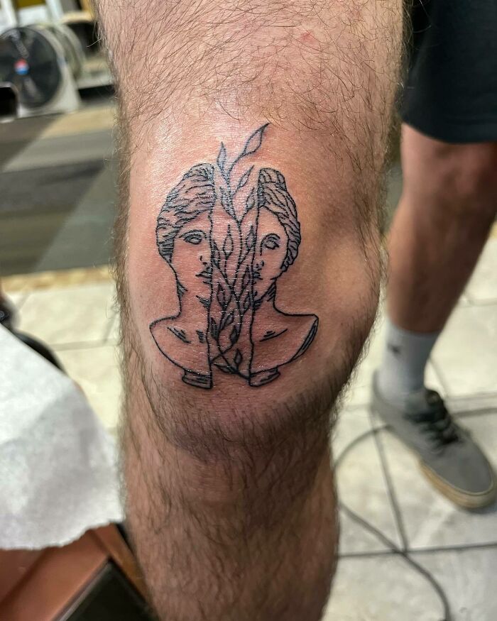Broken in two statue with plant between tattoo 