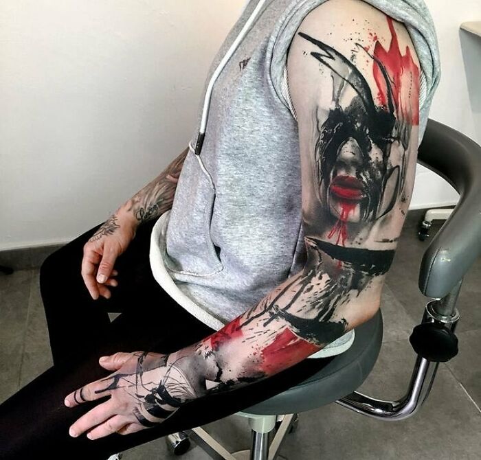 Arm showcasing a striking Trash Polka tattoo with black and red abstract design elements.