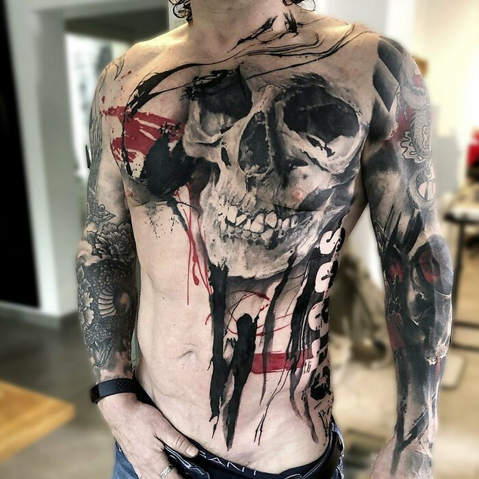 Man with a full torso trash polka tattoo featuring a skull and abstract designs in red and black.