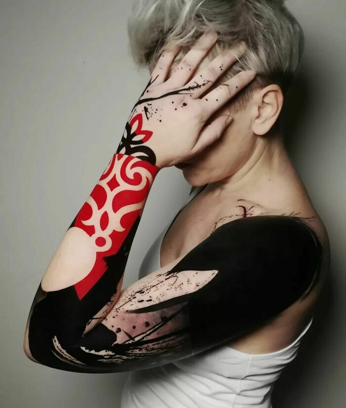 Person with a vibrant Trash Polka tattoo covering their arm, blending red and black ink patterns.