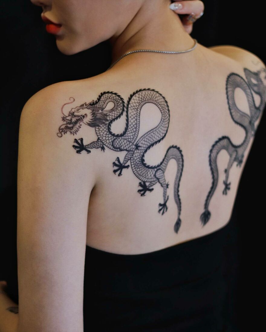 twin black ink dragon tattoos on back facing in different directions