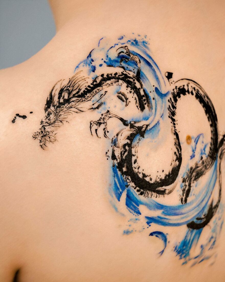 Black and blue colored dragon tattoo on the back side of shoulder