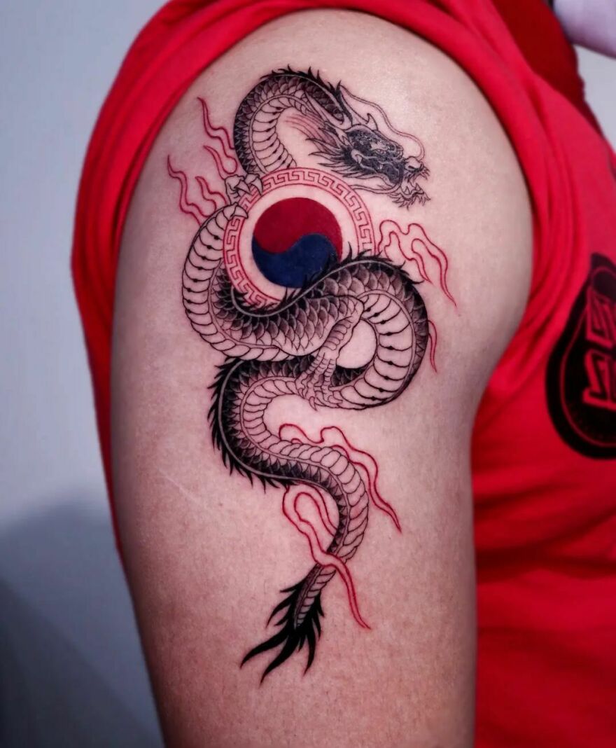 a shoulder tattoo of a dragon with a taeguk mark in red and black ink