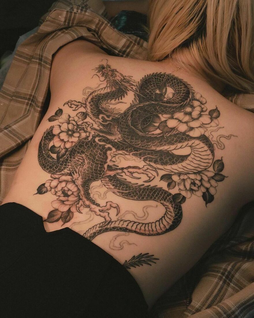black ink tattoo of a dragon and flowers on the back of a lying woman