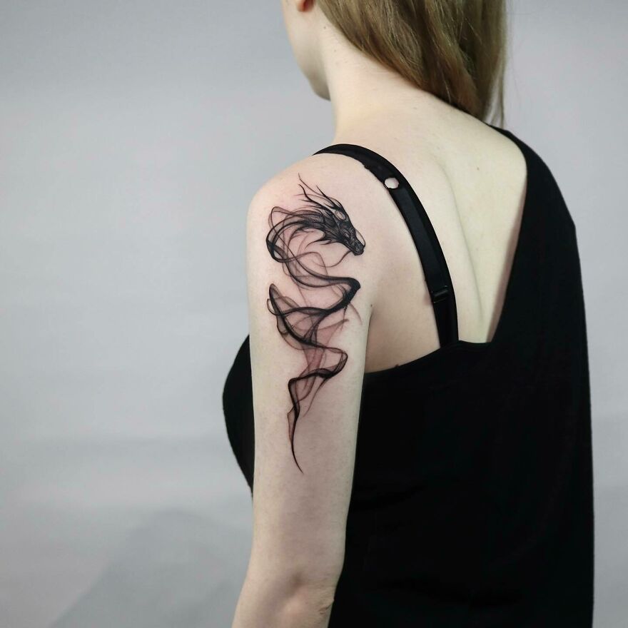 a freeflow style tattoo of a dragon in black ink on a woman's shoulder