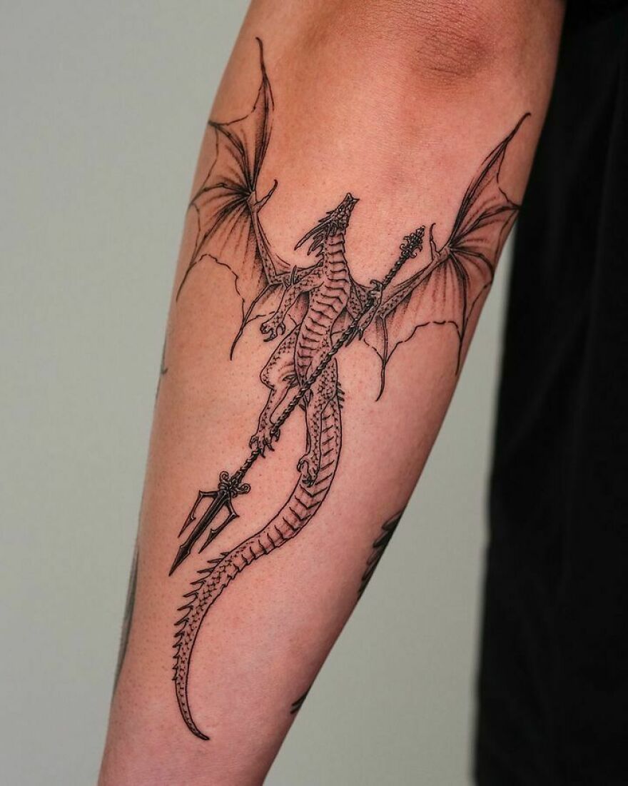 black ink tattoo of a dragon carrying a trident