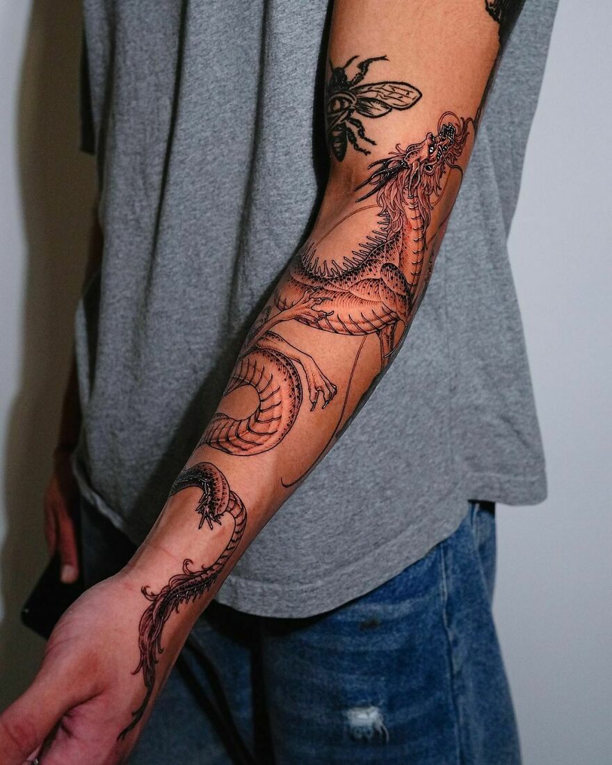 a tattoo of a chinese dragon looking upwards on forearm