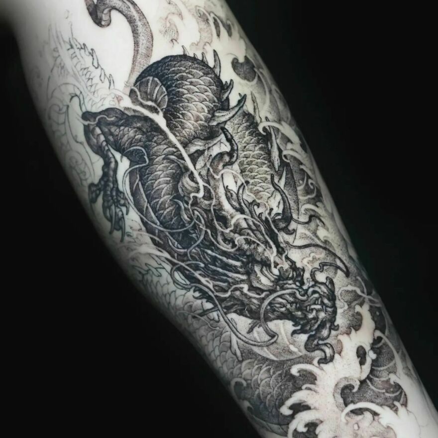 black ink tattoo of a dragon on top of waves