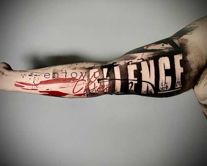 Arm with a Trash Polka tattoo featuring abstract elements and the phrase "enjoy the silence" in bold, stylized lettering.