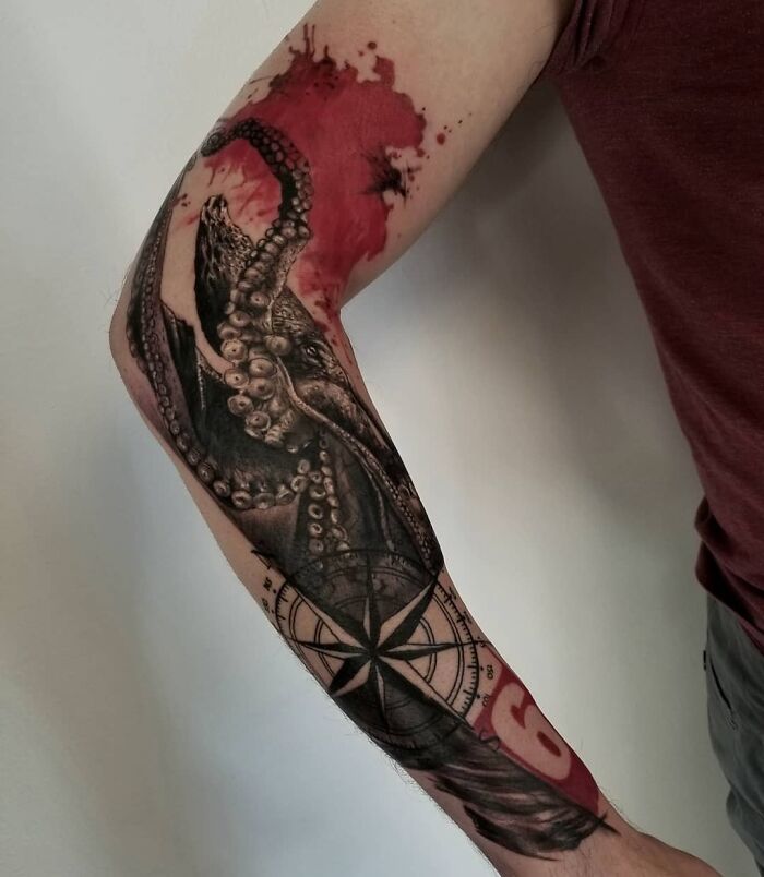 A striking Trash Polka tattoo featuring octopus tentacles and a compass with red ink highlights on a person's arm.