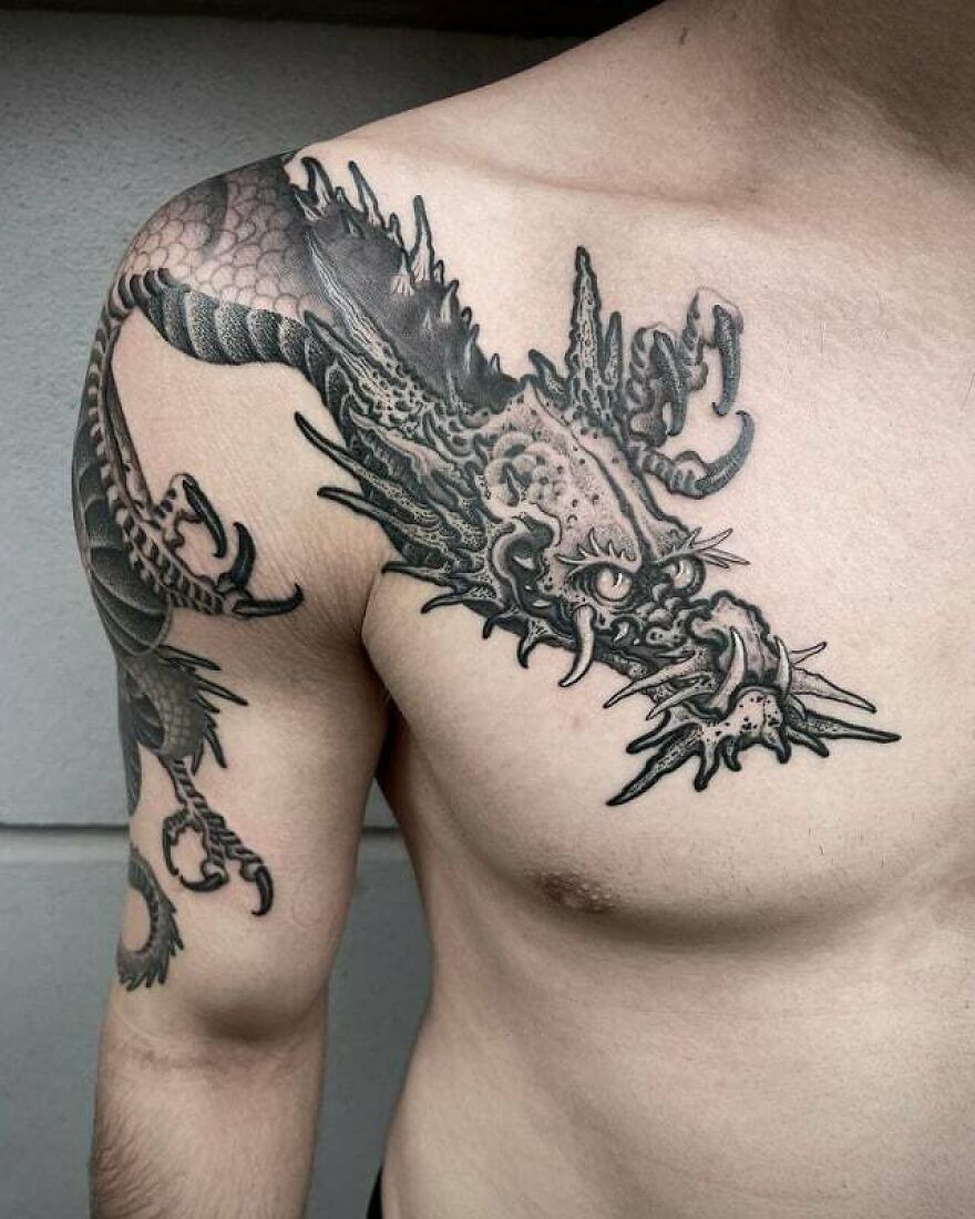 tattoo of a grinning dragon from across the shoulder to the chest