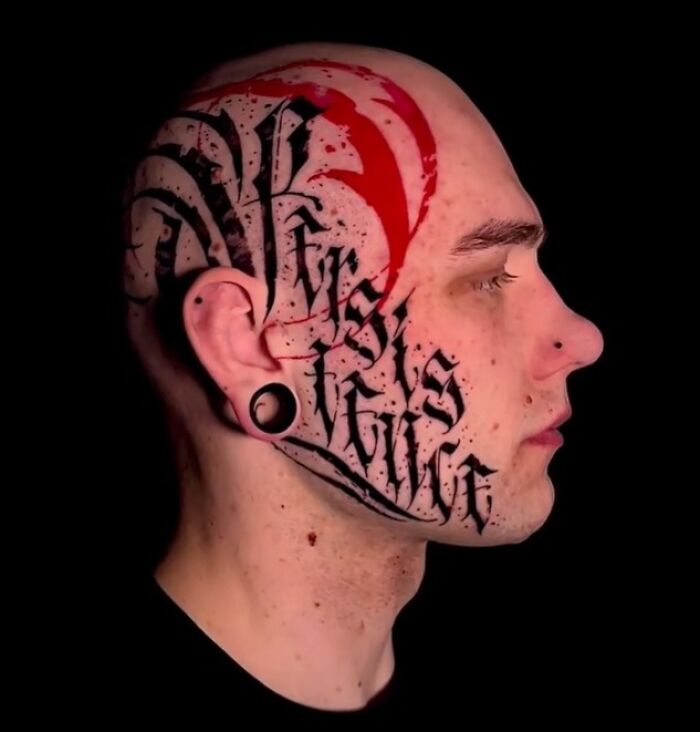 Side profile of a person with intricate Trash Polka tattoo covering the head and face, featuring bold black and red designs.