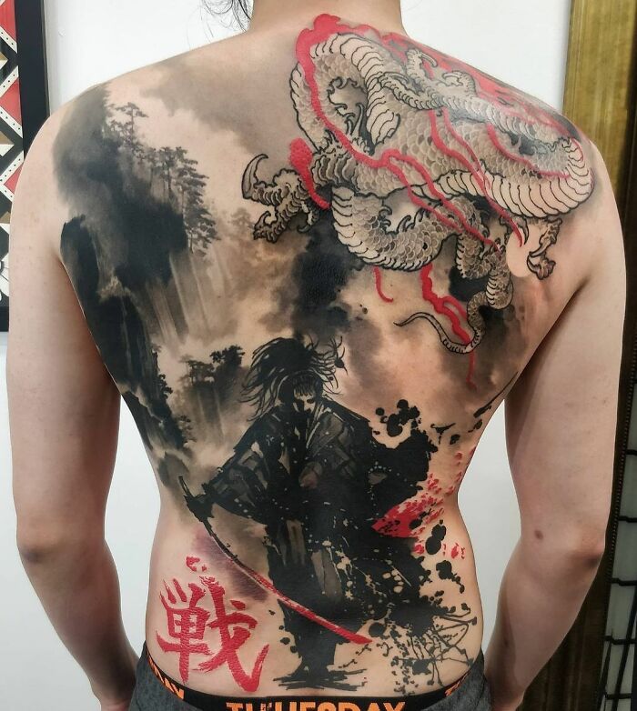 Back tattoo in Trash Polka style featuring a dragon and samurai with bold red and black elements.