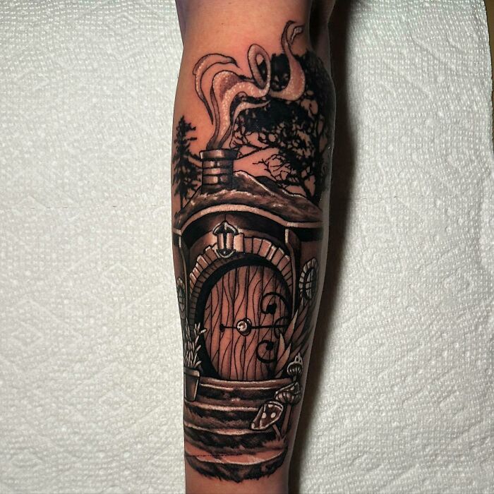 Tattoo of a Hobbit door from Lord of the Rings on forearm, featuring detailed woodwork and surrounding foliage.