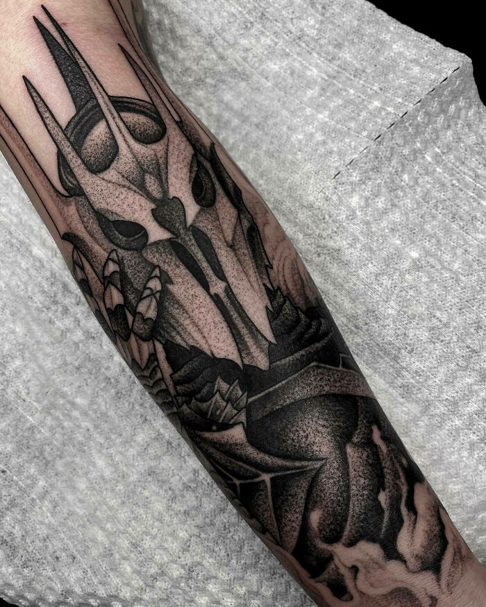 Lord of the Rings tattoo featuring a detailed black and gray design of Sauron's helmet on an arm.