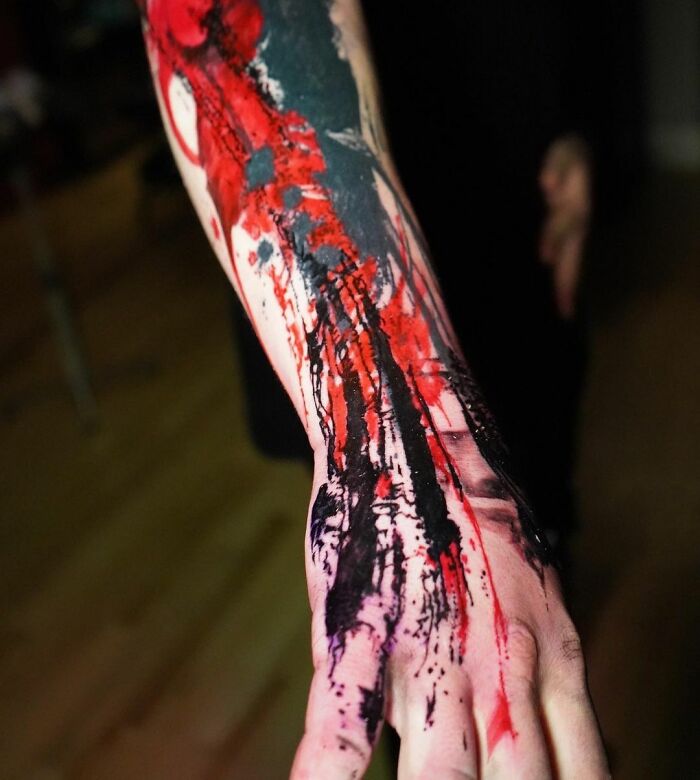 Close-up of a Trash Polka tattoo design with bold red and black ink on a person's forearm.