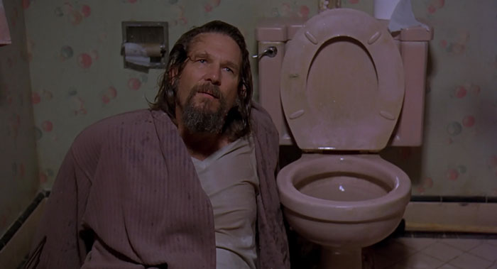Lebowski sitting on the floor near the toilet 