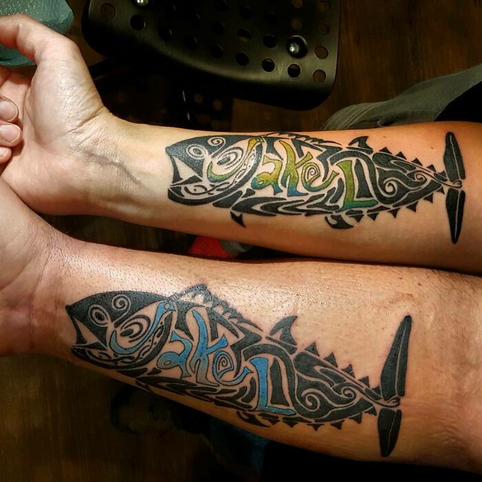 Tribal tattoo design featuring two stylized fish with intricate patterns on forearms.