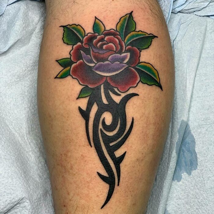 Colorful rose and tribal tattoo on a forearm, showcasing intricate black swirls and vibrant petals.