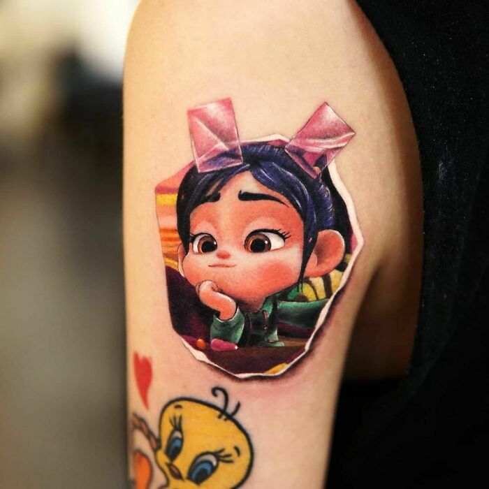 Tattoo of pop culture character on an arm, featuring a girl with a pink bow, symbolizing popular culture art.
