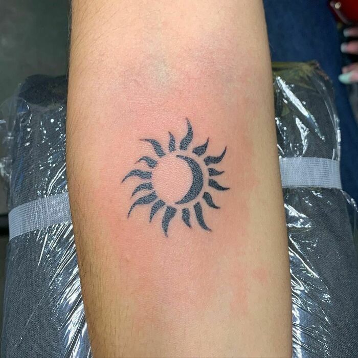 Tribal tattoo of a sun and crescent moon design on an arm.