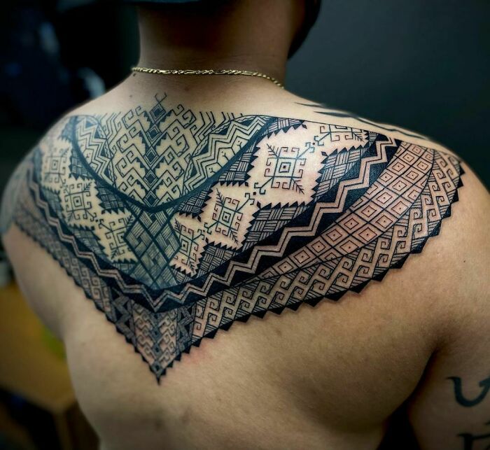 Upper back adorned with an intricate tribal tattoo design featuring geometric patterns and bold lines.