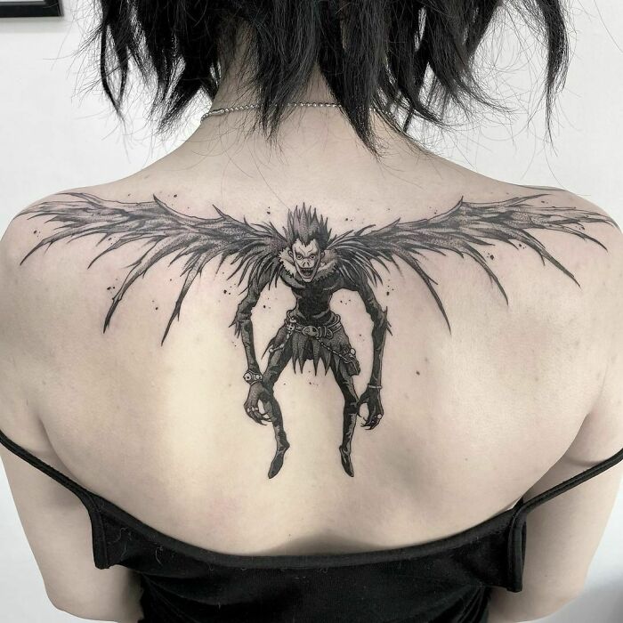 Pop culture tattoo of a winged character spanning across a person's upper back, showcasing intricate black ink detailing.