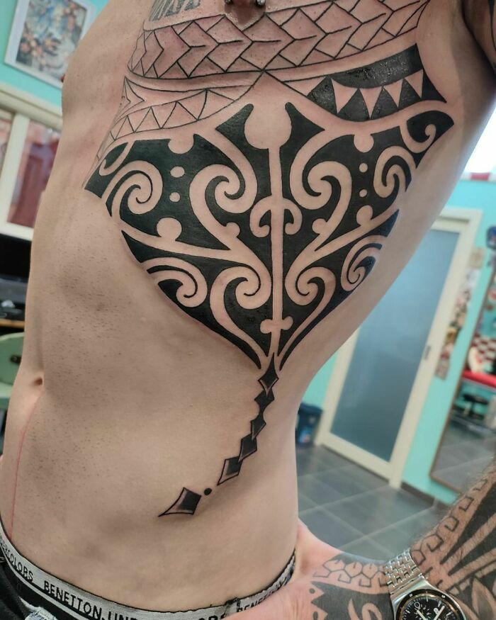 Person with intricate tribal tattoo design on their side in a tattoo studio setting.