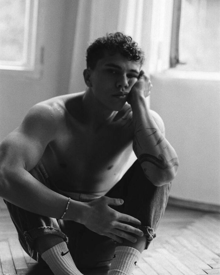 Shirtless man sitting on the floor, showcasing an arm tattoo. Shirtless man sitting on the floor, showcasing an arm tattoo.