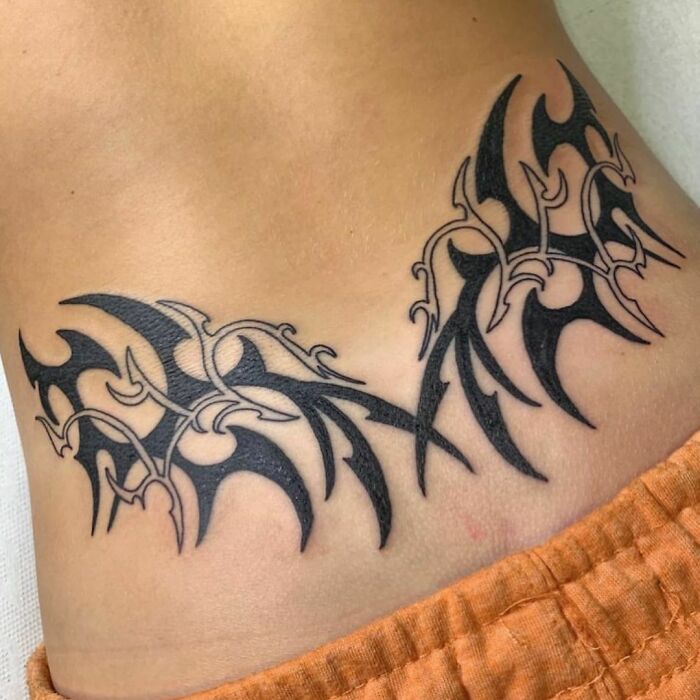 A black tribal tattoo design on a person's side above orange pants.