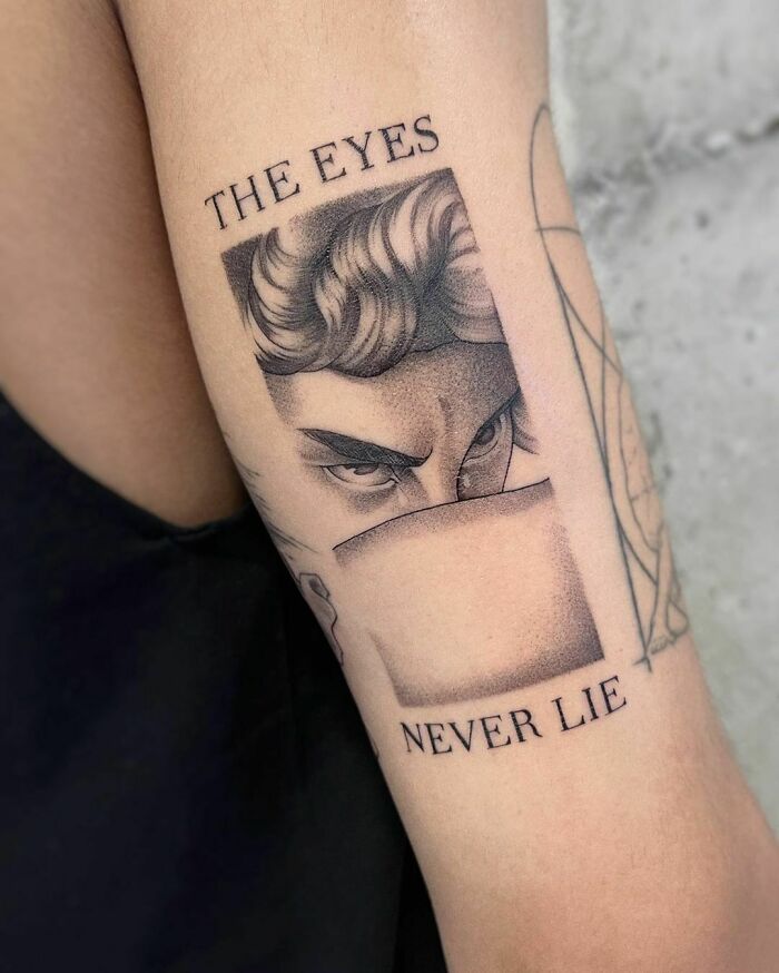 Pop culture tattoo on arm, featuring intense eyes and text "The Eyes Never Lie" in a black and gray design.
