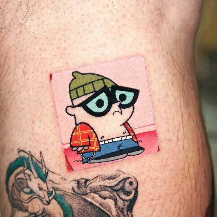 Pop culture tattoo featuring a cartoon character with glasses, a beanie, and a red plaid shirt, alongside a dragon design.