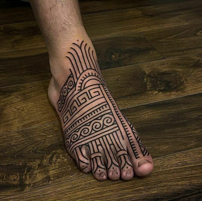 A foot showcasing an intricate tribal tattoo design with geometric patterns on a wooden floor.