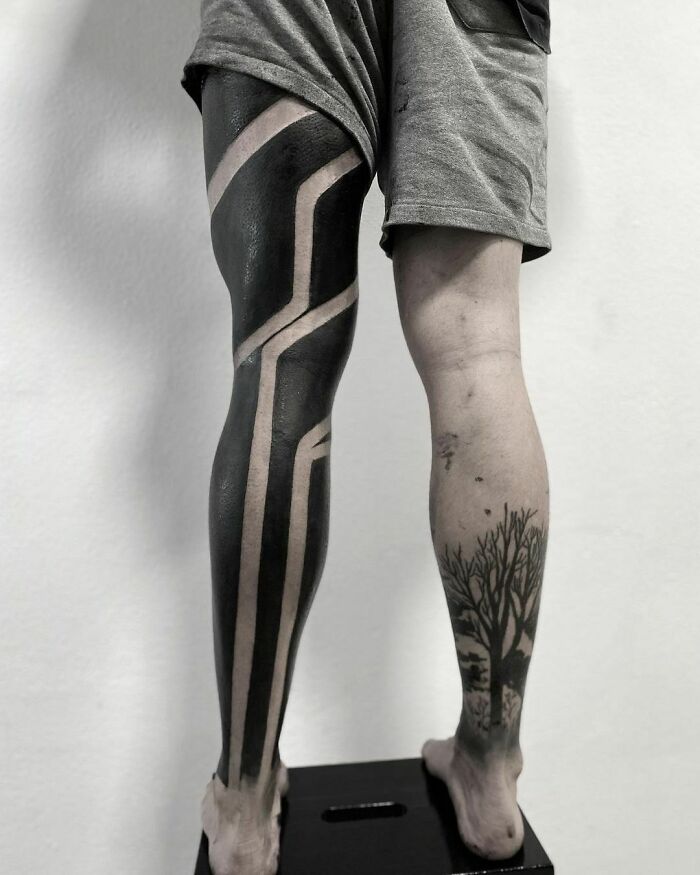 Close-up of tribal tattoo design on a person's leg, featuring bold black and negative space patterns.