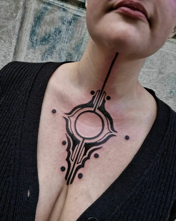 Close-up of a tribal tattoo design on a person's neck and chest, featuring circular and linear patterns.
