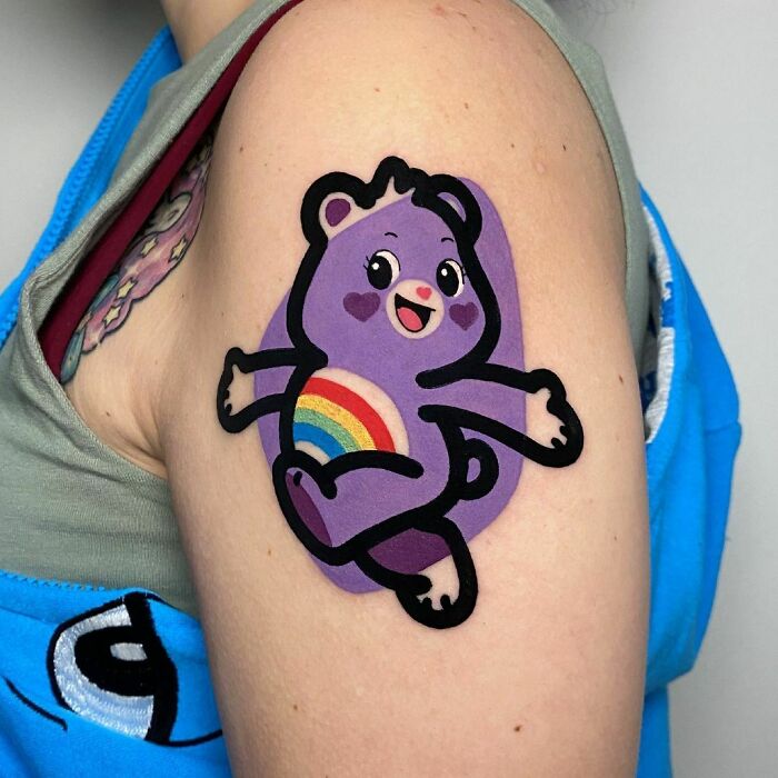 Tattoo of a purple cartoon bear with a rainbow belly on an arm, representing pop culture tattoos.