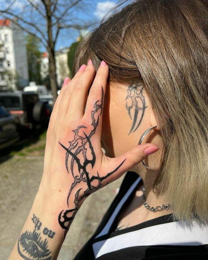 Woman with tribal tattoos on hand and neck, wearing hoop earring, outdoors.