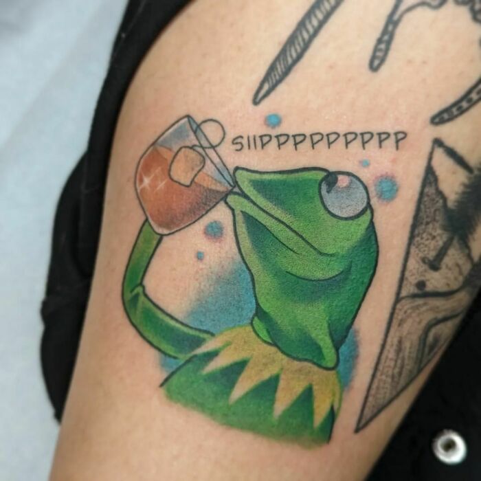 Pop culture tattoo of a green frog sipping tea, with "SIP" text, inked on an arm.