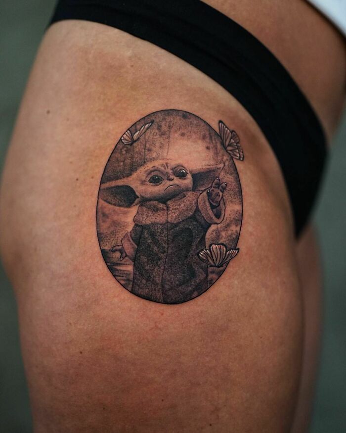 Pop culture tattoo featuring a small, iconic creature with butterflies on a person's thigh.