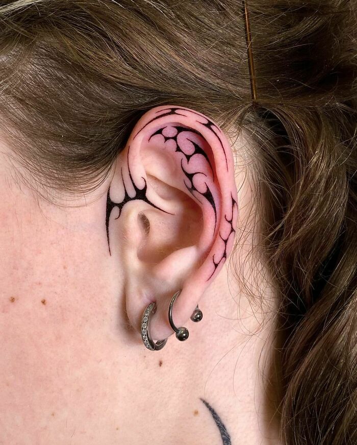 Tribal tattoo design on ear, featuring swirling patterns and piercings.