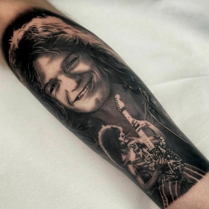 Pop culture tattoo of a smiling guitarist with long hair, holding an electric guitar, artistically detailed on an arm.