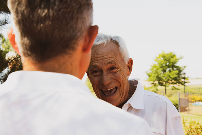 Grandpa sharing wise and funny advice with a man outdoors, smiling and enjoying a warm conversation in nature.
