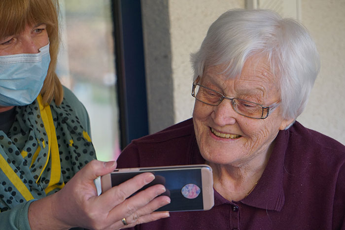 Woman showing videos and pictures on phone to smiling grandmother, sharing moments full of wise and funny advice from grandparents