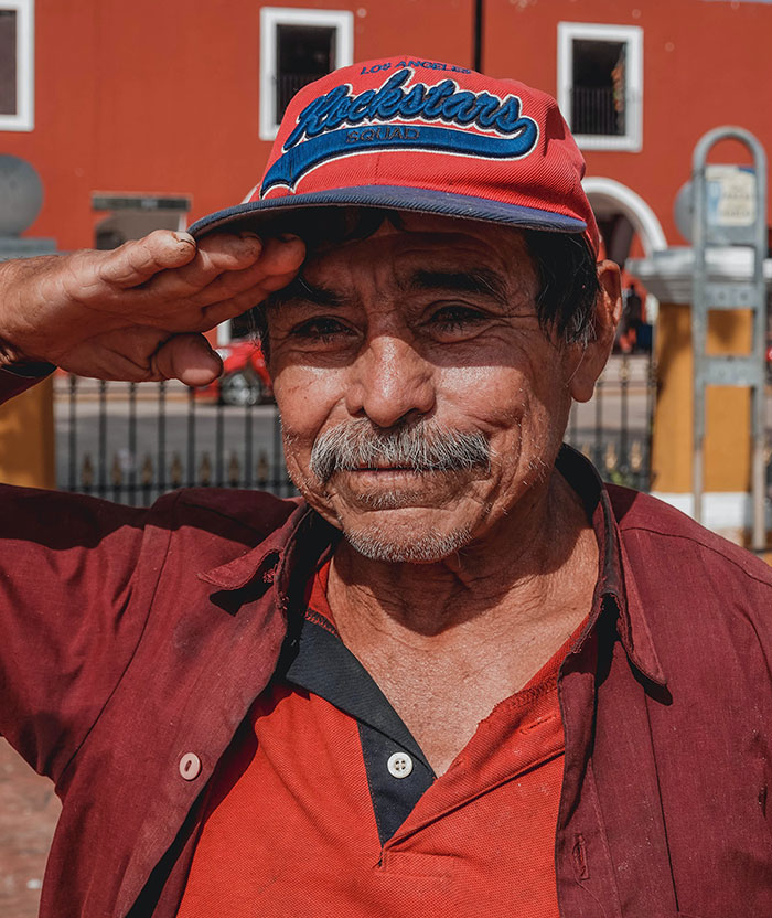 Elderly man in red shirt and cap saluting, representing wise and funny advice from grandparents.